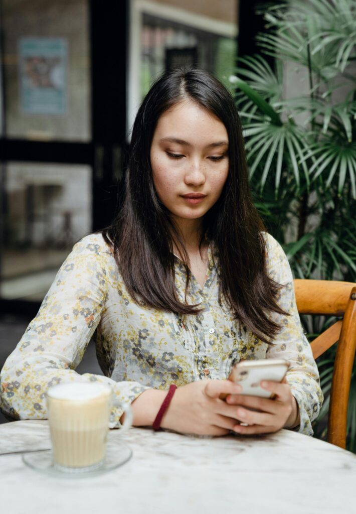 Young woman using smartphone while relaxing at a café. Latte on the table.