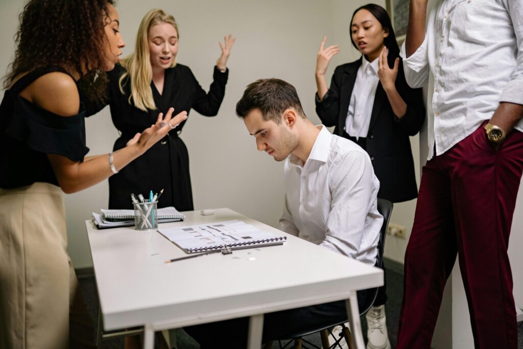 A team confronts a stressed colleague at a tense office meeting, highlighting workplace dynamics.