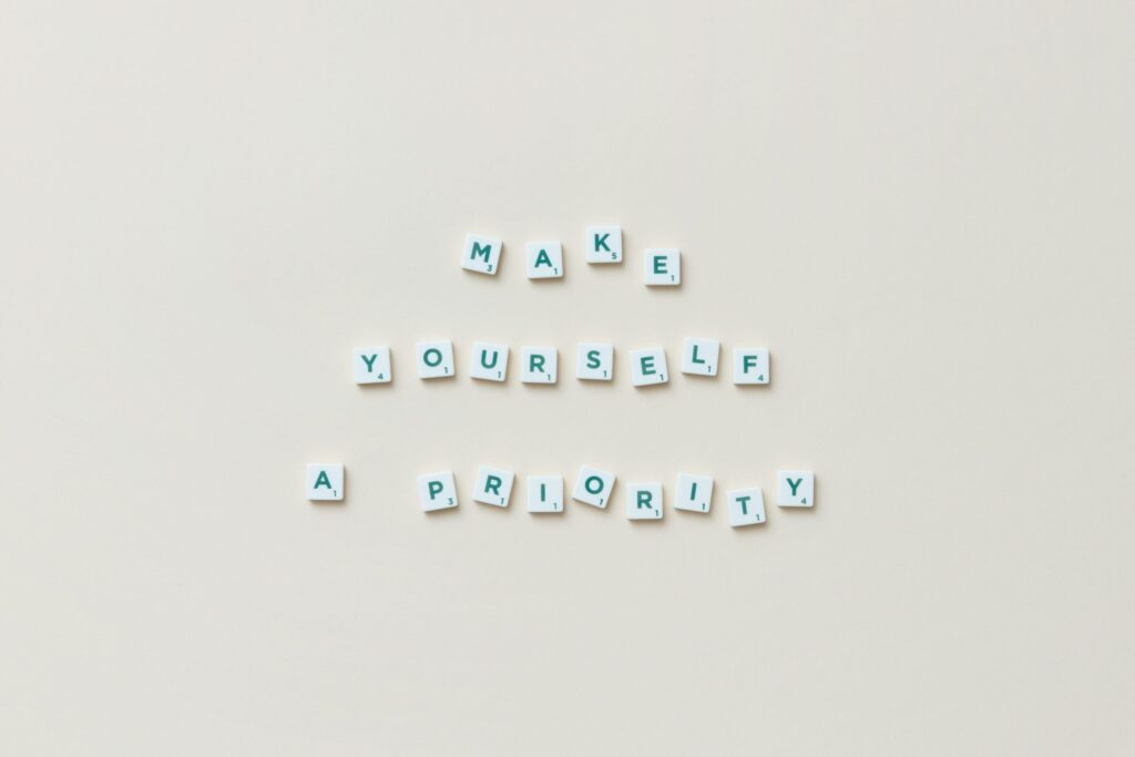 Top view of motivational phrase 'Make Yourself a Priority' with Scrabble tiles on white background.