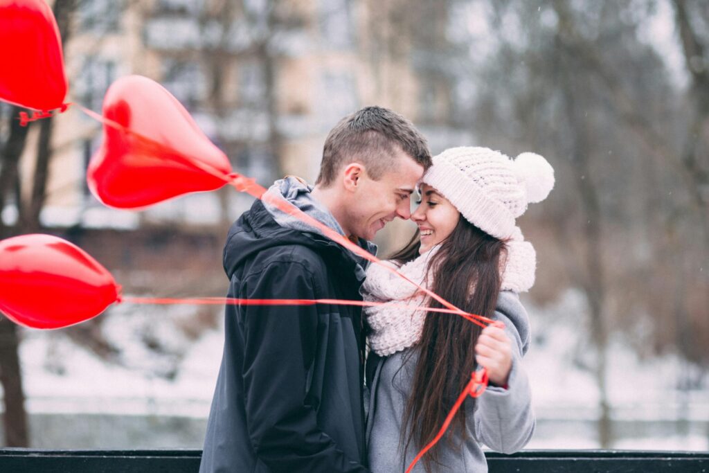 Young couple embracing with red heart balloons outdoors in winter, sharing a joyful moment.